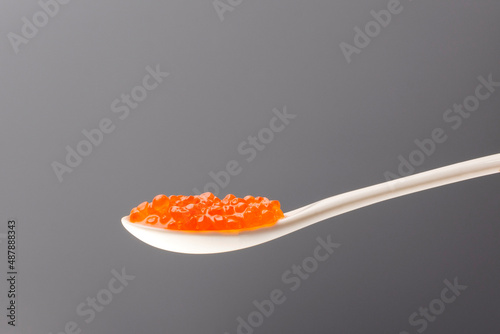 red fish caviar in a white ceramic spoon on a gray background