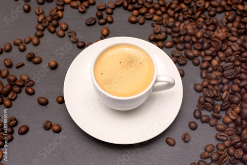 white cup with espresso coffee on a saucer with coffee beans on a dark background © Valeriy Volkonskiy