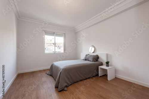 Bedroom with gray bed and bedspread with aluminum window and white furniture on wooden floor