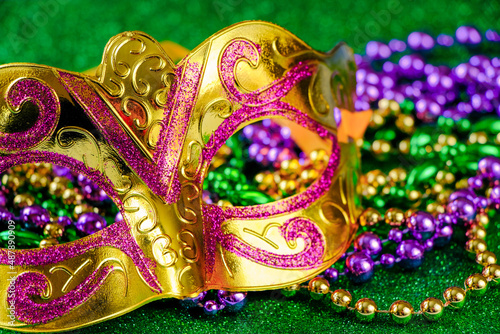 Carnival mask and colorful beads on green shiny background. Mardi Gras concept. Fat Tuesday symbol.