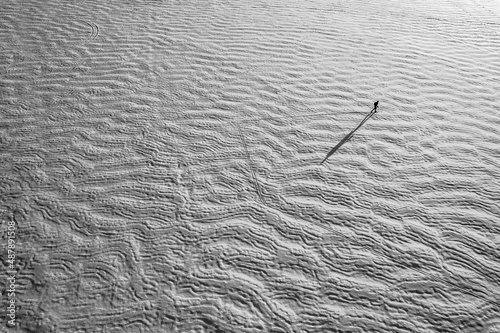Aerial view of tiny lone skier on frozen snow covered textured lake