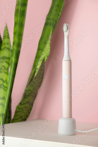 New modern ultrasonic toothbrushes. Dental care supplies with green leaves on pink pastel background. Oral hygiene, gum health, healthy teeth. Dental products Ultrasonic vibration toothbrush.