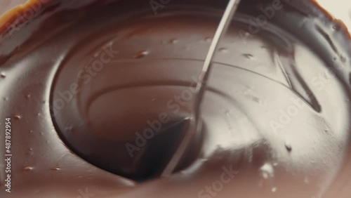 Macro view of dark melted chocolate, satiny smooth liquid texture, swirled with a spoon.