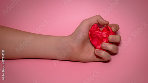 hand holds red Crumpled paper heart heart on pink background. Paper heart in the palm. Heart health concept