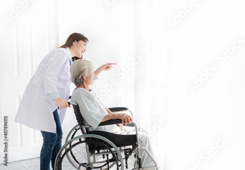 asian female doctor talk about rehabilitation process with old stroke patient near window, they feeling happy and smile, old asian people sitting on wheelchair, elderly healthcare