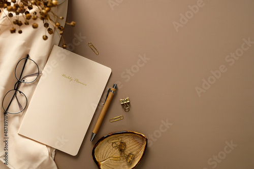 Home office desk table with weekly planner, pen, office stationery, glasses, beige cloth, dried flowers. Elegant, aesthetic feminine workspace.