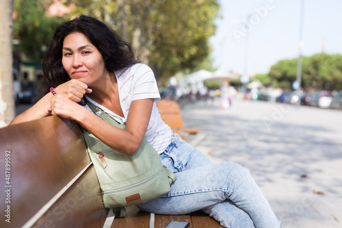 Black-haired oriental woman resting on bench in urban park.
