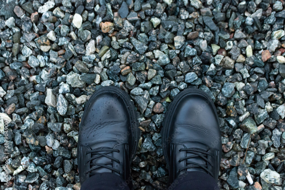 Feet in black boots on a dark small rocks. Close-up. Top view Feet in black boots on a dark small rocks. Close-up. Top view