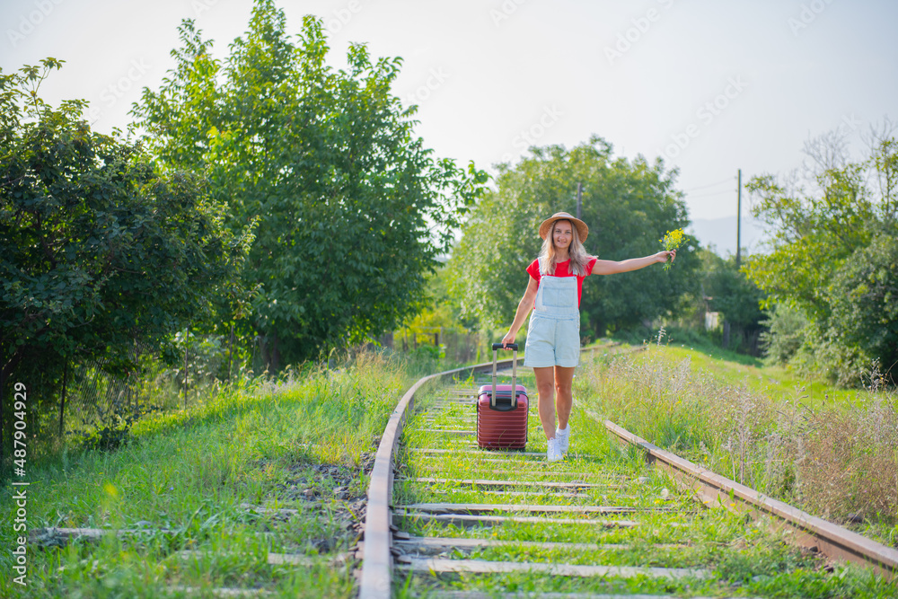 a woman in a hat and a suitcase walks along the sleepers