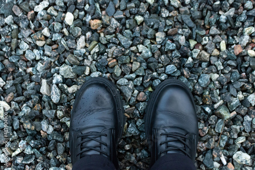 Feet in black boots on a dark small rocks. Close-up. Top view