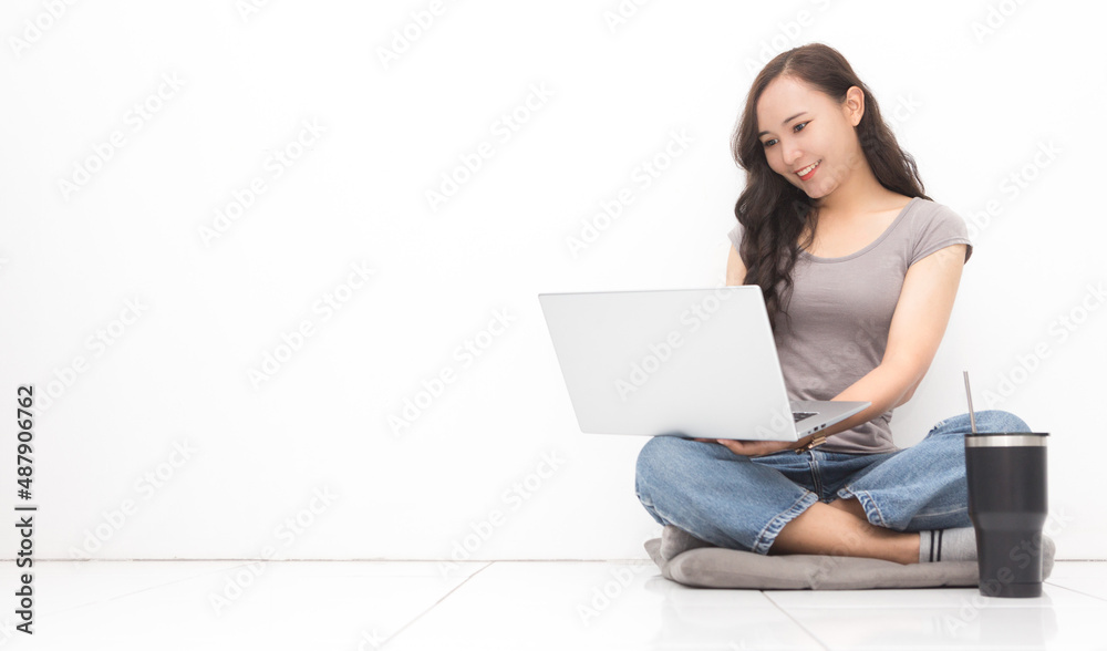 Beautiful Asian woman wearing grey casual shirt using laptop on white background and copy space. Cute Asian woman sitting on the floor room relaxing for work from home concept Beautiful Asian woman wearing grey casual shirt using laptop on white background and copy space. Cute Asian woman sitting on the floor room relaxing for work from home concept