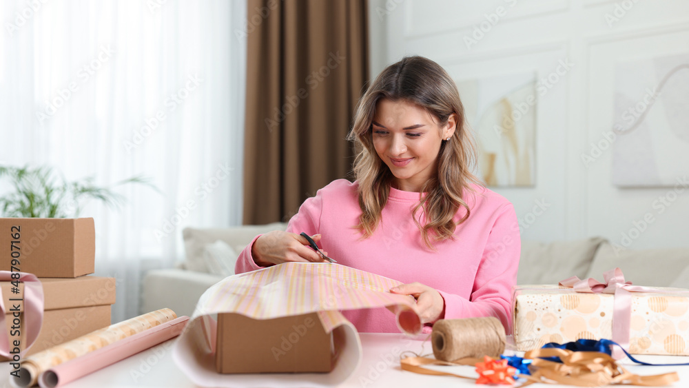 Beautiful young woman wrapping gift at table in living room Beautiful young woman wrapping gift at table in living room