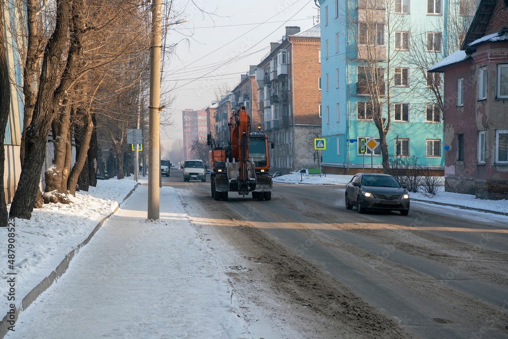 Obraz premium Orange excavator moving along the city winter road.