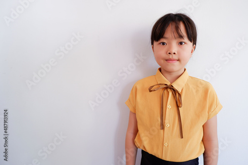 A photograph of a young woman standing upright with a bright face in a yellow shirt on a plaster background.