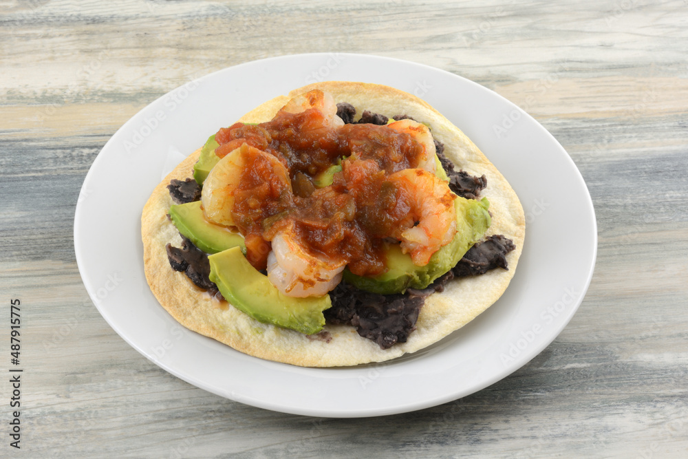 Shrimp and black bean tostada with avocado and salsa on white plate Shrimp and black bean tostada with avocado and salsa on white plate