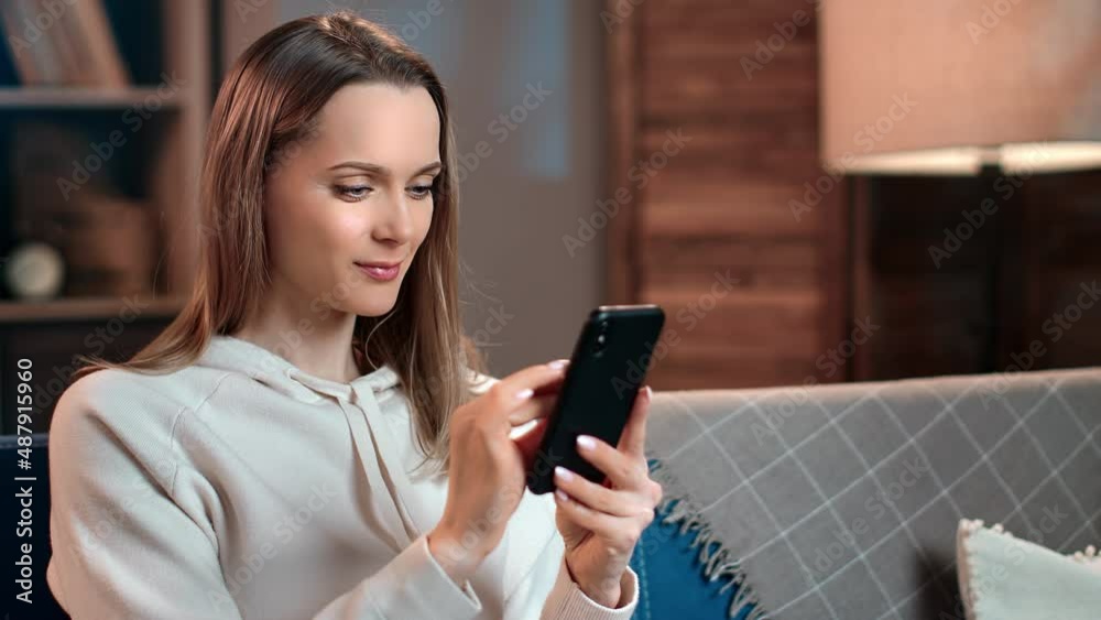 Happy domestic woman chatting online dating application use smartphone on couch evening living room Happy domestic woman chatting online dating application use smartphone on couch evening living room