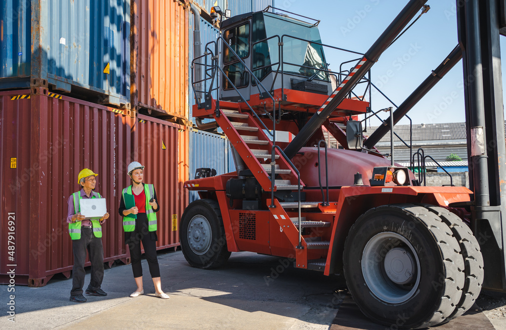Female engineer and foreman standing at stacking forklift preparing import export goods at shipping terminal. Senior worker holds notebook checking containers loading data. Container handler concept.