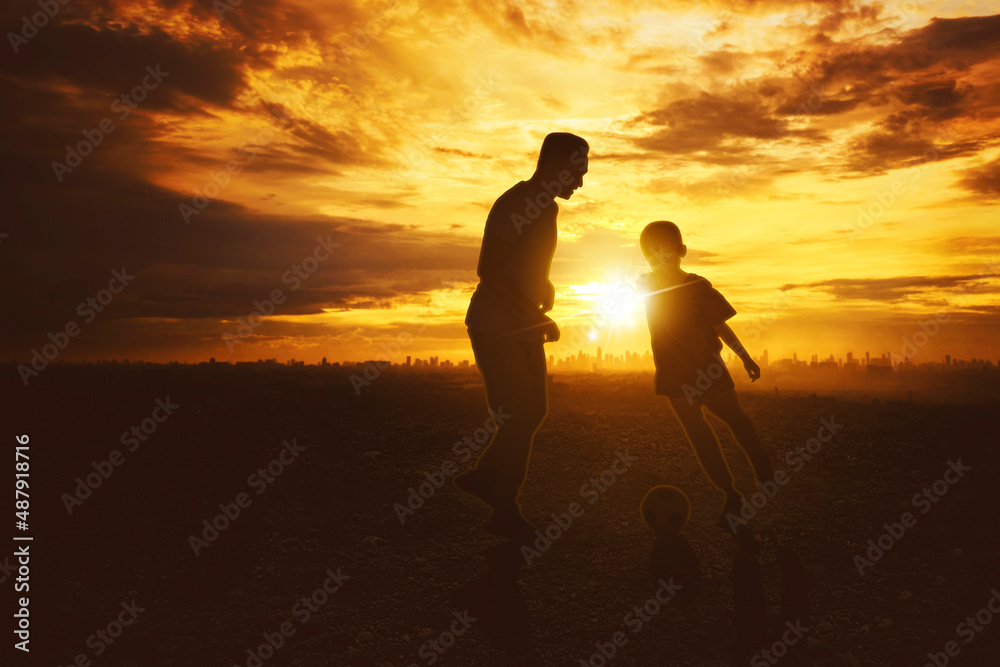Silhouette of father plays football with son at park