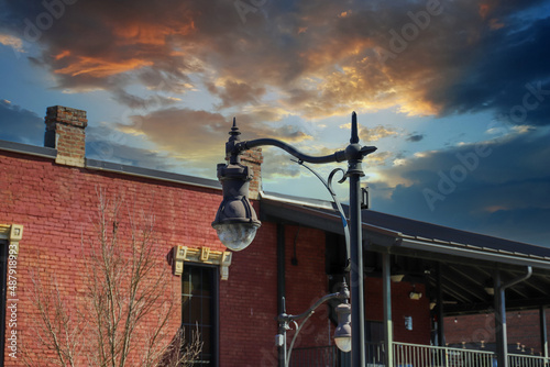 a tall curved black light post in front of a red brick building with a black metal balcony with bare winter trees and blue sky and powerful clouds at sunset in Douglasville Georgia USA photo