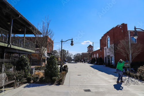 a shopping center with red brick buildings, tall curved black light posts, metal benches, bare winter trees and lush green plants with blue sky in Douglasville Georgia USA photo