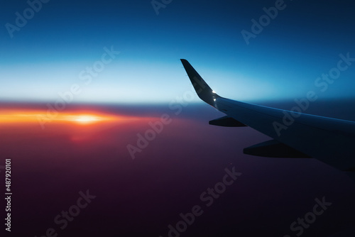 View from the window of the aircraft on the wing over the colorful sunset and illuminated vivid clouds