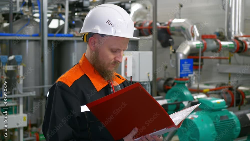 Technological engineer in a white helmet makes entries in the journal during the operation of the equipment of the industrial complex. The work of an engineer at an oil refinery. Technological engineer in a white helmet makes entries in the journal during the operation of the equipment of the industrial complex. The work of an engineer at an oil refinery.