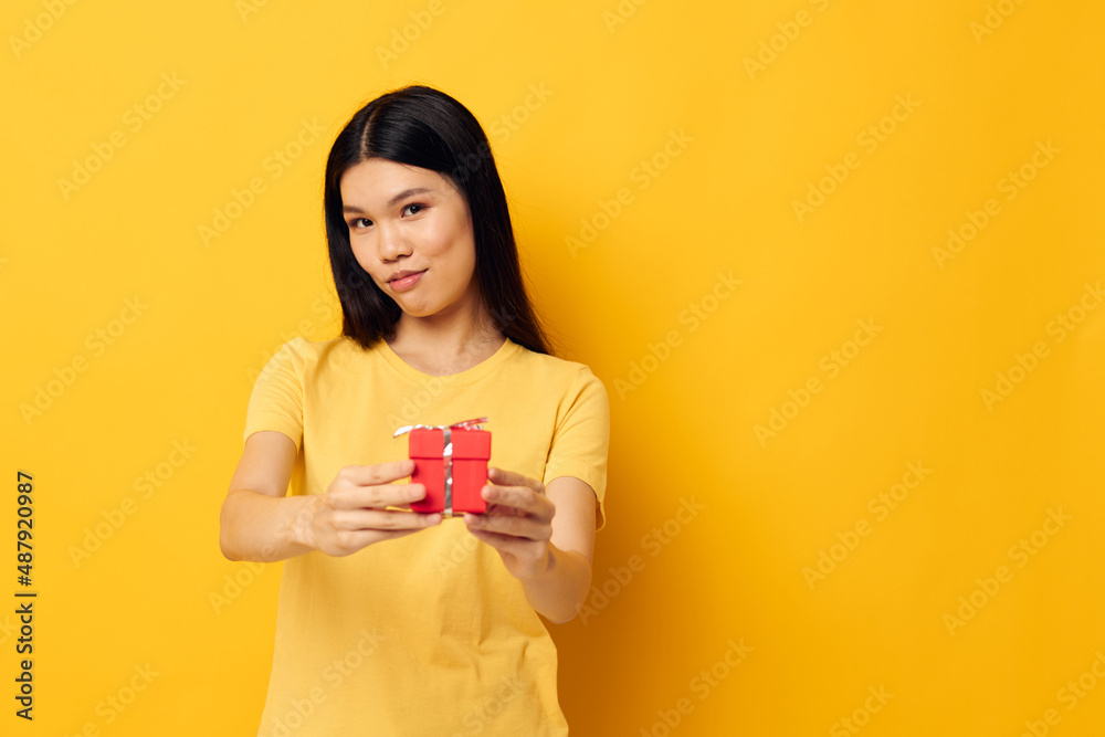 Portrait Asian beautiful young woman holding a gift box in his hands posing yellow background unaltered