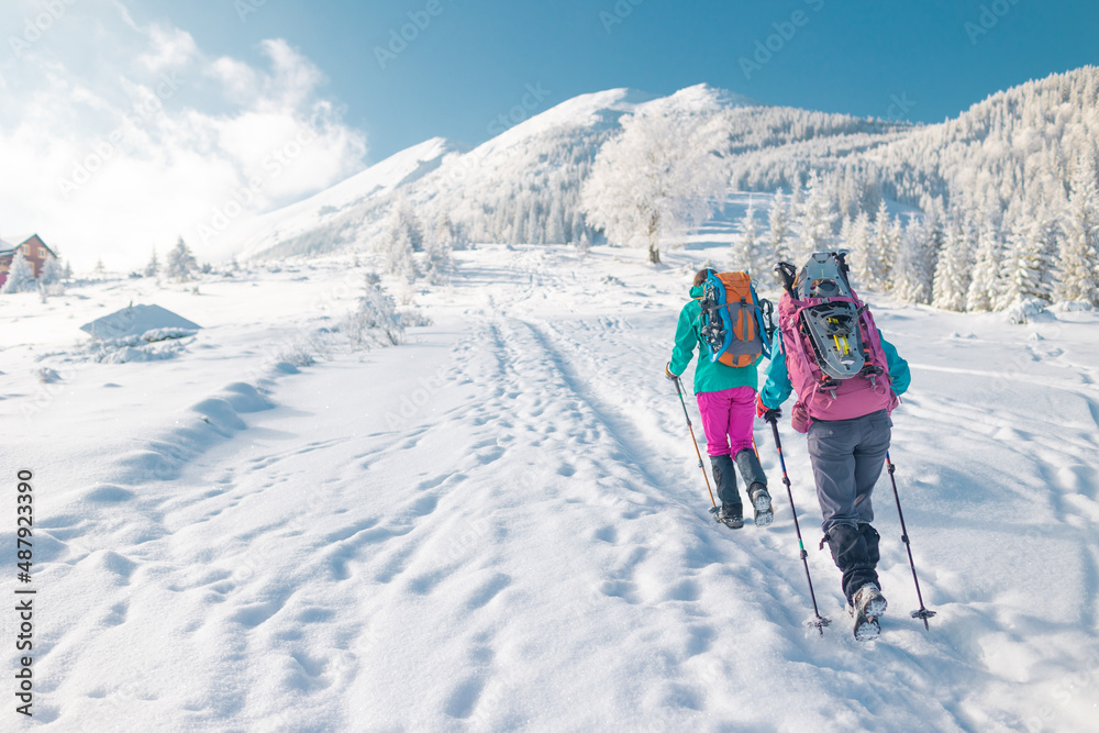 Two women walk with snowshoes on the backpacks in winter trekking