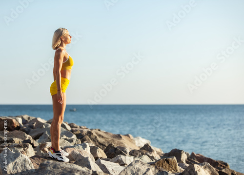 Portrait of a muscular young woman standing on stones at the beach