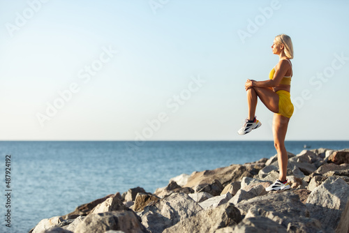 Young athletic woman practicing leg stretching while standing on stones at the beach