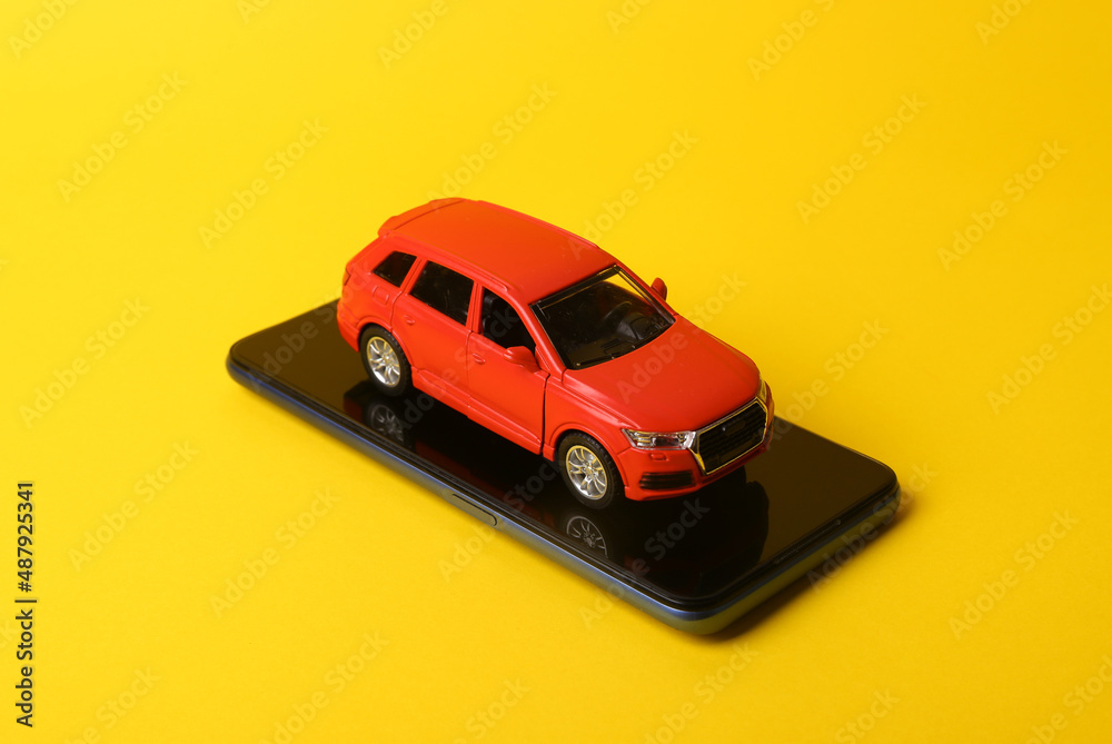 Toy car model with smartphone on yellow background.