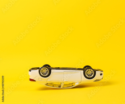 Upside down model of a toy car on a yellow background. Car accident