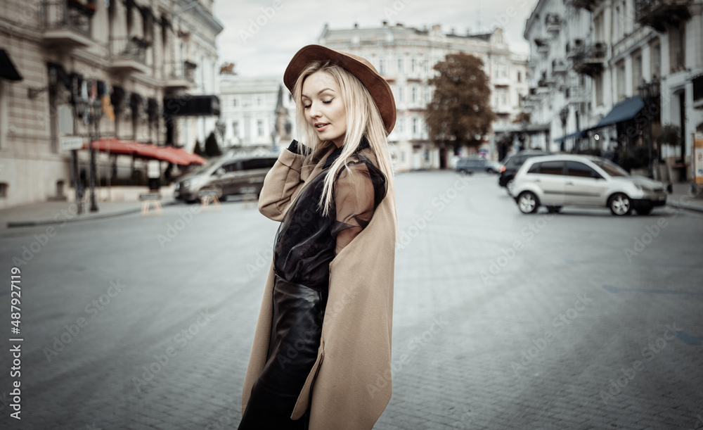 Portrait of young stylish blonde woman in autumn coat and felt hat in a European city. Beautiful attractive girl