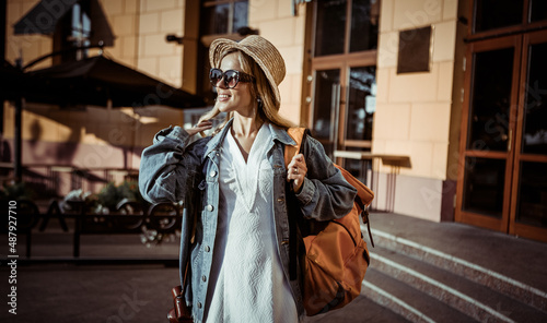 Portrait of millennial woman tourist in hat and sunglasses with backpack in the city.