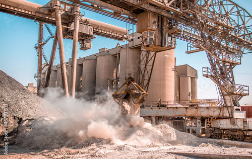 Modern technology of the bucket moves gravel, work at a cement plant. Technological work on the production of cement. Working atmosphere with copy space. Heaps of sand and soil raw materials.
