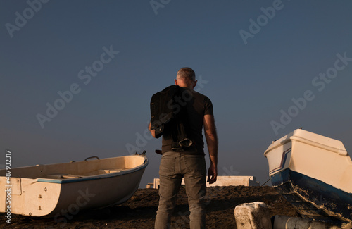 Rear view of adult man on beach with fishing boat during sunset. Almeria, Spain