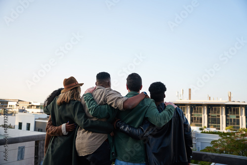 Trendy, Diverse group of friends standing together on rooftop at party in the city. Looking at beautiful view