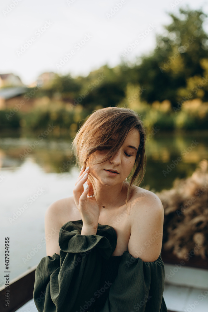 a young woman in a dark green off-the-shoulder dress sits in an old wooden boat. a beautiful girl poses in a boat in the middle of a lake or river at sunset. evening boat trip on the canal.
a young woman in a dark green off-the-shoulder dress sits in an old wooden boat. a beautiful girl poses in a boat in the middle of a lake or river at sunset. evening boat trip on the canal.