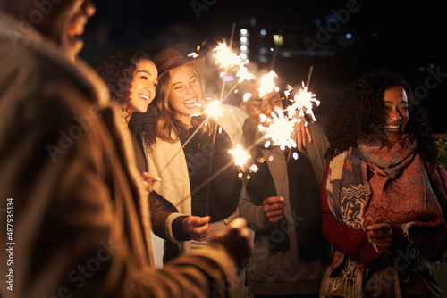 Multi-cultural group of friends laughing while lighting sparklers at a trendy rooftop party photo