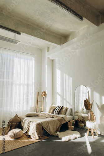 bedroom interior with white walls and large windows with white tulle. spacious bright bedroom filled with natural light. loft room with high ceilings and plenty of blankets and pillows on the bed.	
