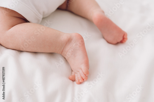 legs of newborn baby on white sheet close-up, baby learns to crawl
