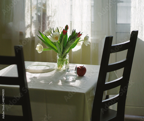 A bouquet of tulips on the table, white dishes, the table is covered with a white tablecloth.