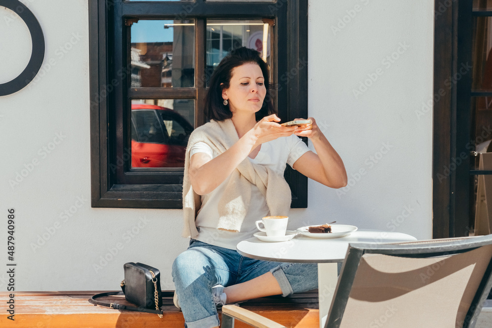 Young woman in casual  clothes sits in a cafe and takes pictures of food with a mobile phone.