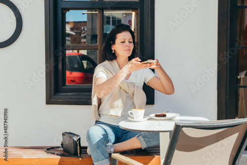 Young woman in casual clothes sits in a cafe and takes pictures of food with a mobile phone.