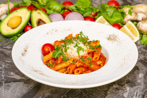 Penne pasta in tomato sauce, tomatoes decorated with parsley on a wooden background