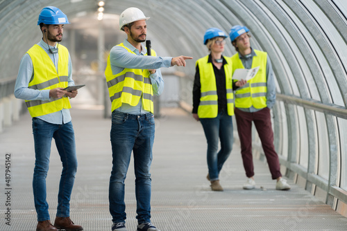 workers in walkway wearing high-visibility vests one talking into microphone