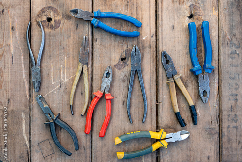 a lot of pliers with rubber handles of different colors on a wooden background. The concept of repair or construction. Top view.