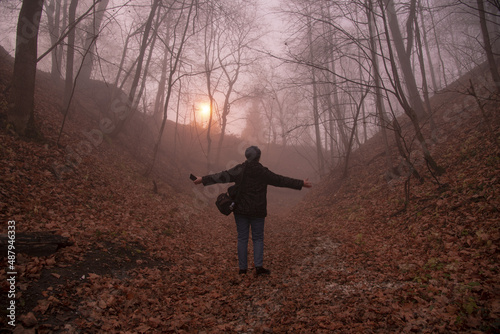 A female silhouette in the fog on a road covered with fallen leaves.