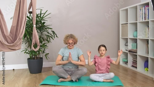 Grandma and a little are sitting on a blue mat and meditating.