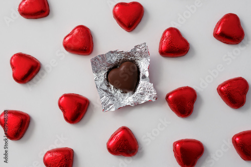 Love, relationship and broken heart concept - close up of wrapped and unwrapped heart shape chocolate candies in red foil over white